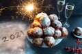 Happy New Year with the year 2021 written icing sugar next to a bowl of oliebollen (Dutch dough fritters)