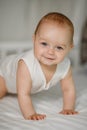 A happy newborn baby crawls on the bed and smiles.