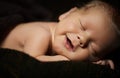 Happy newborn baby smiling in his sleep on a dark
