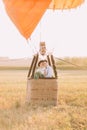 Happy newlyweds in the basket of the airballoon. The groom is hugging the bride back. The field composition.