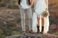 Happy newlyweds with beautiful field bouquet standing on rock outdoors