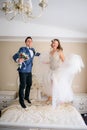 Happy newlyweds jump on bed in hotel room