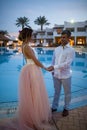 Happy newlyweds stand holding hands next to the swimmimg pool during the honeymoon Royalty Free Stock Photo