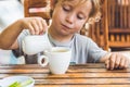 Happy nice boy pours honey into the tea in summer green garden. Royalty Free Stock Photo