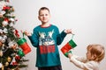 A happy nine-year-old boy holds socks for New Year`s gifts near a Christmas tree on white background. boy in pajamas with a