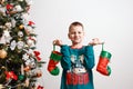 A happy nine-year-old boy holds socks for New Year`s gifts near a Christmas tree on white background. boy in pajamas with a