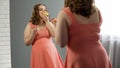 Happy obese lady satisfied with her body eating sweet donuts in front of mirror