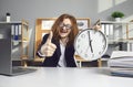 Happy office worker sitting at desk, holding clock that says it's 5 pm and giving thumbs-up