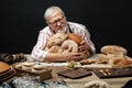 Happy old baker looking at camera and smiling while hugging loaves of bread Royalty Free Stock Photo