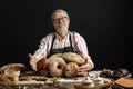 Happy old baker looking at camera and smiling while hugging loaves of bread