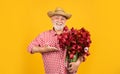 happy old bearded man in hat presenting spring tulip flowers on yellow background