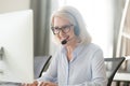 Happy old businesswoman in headset making call looking at computer Royalty Free Stock Photo