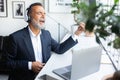 Happy old caucasian man in suit and wireless headphones resting, singing at table in office Royalty Free Stock Photo