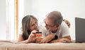 Happy old caucasian wife hugging husband showing credit card, lies on bed with laptop, enjoy online shopping Royalty Free Stock Photo