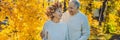 Happy old couple having fun at autumn park. Elderly man wearing a wreath of autumn leaves to his elderly wife BANNER