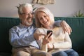 Happy old couple holding smartphone looking at cellphone screen laughing