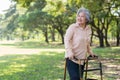 Happy old elderly Asian woman uses a walker for osteoarthritis rehabilitation physiotherapy in park. Concept of happy retirement Royalty Free Stock Photo