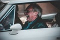 Happy old male laughing while driving an old car during the Reggae festival