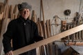 Happy old man in black jacke holds in his hands wooden plank, smiling and looking at the camera