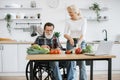 Happy old married man in wheelchair and wife prepare healthy salad. Royalty Free Stock Photo