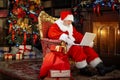 Happy old Santa Claus is sitting in a chair next to the fireplace and the Christmas tree, using a laptop computer. Royalty Free Stock Photo