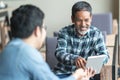 Happy old short beard asian man sitting, smiling and listen to partner that showing presentation on smart digital tablet.