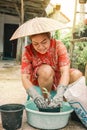 Happy old Thai gardener woman in vietnamese straw hat potting flowers in her garden