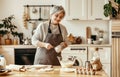 Happy old woman Granny cooks in kitchen kneads dough, bakes cookies