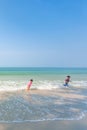 Happy older brother and little sister playing and surfing on white sand beach, light blue sky backgrounds. Summer season. Sunny