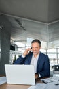 Happy older business man talking on cell phone using laptop in office. Royalty Free Stock Photo