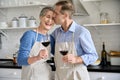 Happy older couple hugging, drinking wine in kitchen celebrating Valentines Day.