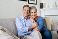 Happy older couple hugging, looking at camera, sitting on couch in apartment. Royalty Free Stock Photo