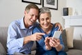 Happy older mature couple enjoying using cell phone sitting on couch at home. Royalty Free Stock Photo