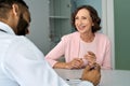 Happy older mature female patient talking to indian male doctor at appointment. Royalty Free Stock Photo