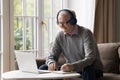 Happy older pensioner man in headphones writing notes at laptop