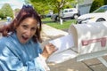 Happy older senior citizen woman looks surprised as she removes a blank white envelope from a white mailbox Royalty Free Stock Photo