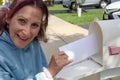 Happy older senior citizen woman smiles as she removes a blank white envelope from a white mailbox Royalty Free Stock Photo