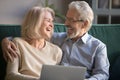 Happy older spouses couple laughing embracing using laptop at home Royalty Free Stock Photo