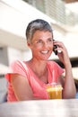 Happy older woman sitting outside with drink and talking on mobile phone Royalty Free Stock Photo