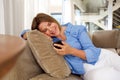 Happy older woman sitting on sofa looking at mobile phone Royalty Free Stock Photo