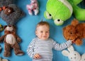 Happy one year old boy lying with many plush toys