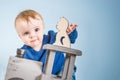 Happy one year old child in a blue sweater plays wooden toys. Blonde baby boy on blue background. Cat and train of wood Royalty Free Stock Photo