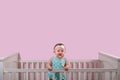 Happy one year old girl standing in her crib wearing polka dots