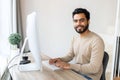 Happy and optimistic Indian man in casual wear using computer in modern office. Successful inspired arabic male Royalty Free Stock Photo