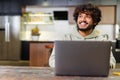 Happy and optimistic Indian man in casual wear using laptop in modern flat. Successful inspired Arabic male entrepreneur Royalty Free Stock Photo