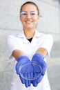 Happy Oriental chemist girl in a white coat, rubber gloves, and goggles holding a Petri dish