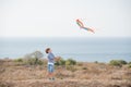 Happy outdoor leisure games by small active caucasian boy with flying kite in air with sea horizon and blue sky in summer Royalty Free Stock Photo