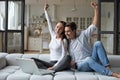 Happy overjoyed couple celebrating online betting bid lottery win sitting on couch at home with raised hands Royalty Free Stock Photo