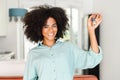 Happy overjoyed young woman with afro hairstyle holding keys with keychain in form of little house indoors. Smiling