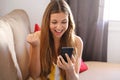 Happy overjoyed young woman holding mobile phone celebrating bid win game app victory sit on sofa at home, excited euphoric Royalty Free Stock Photo